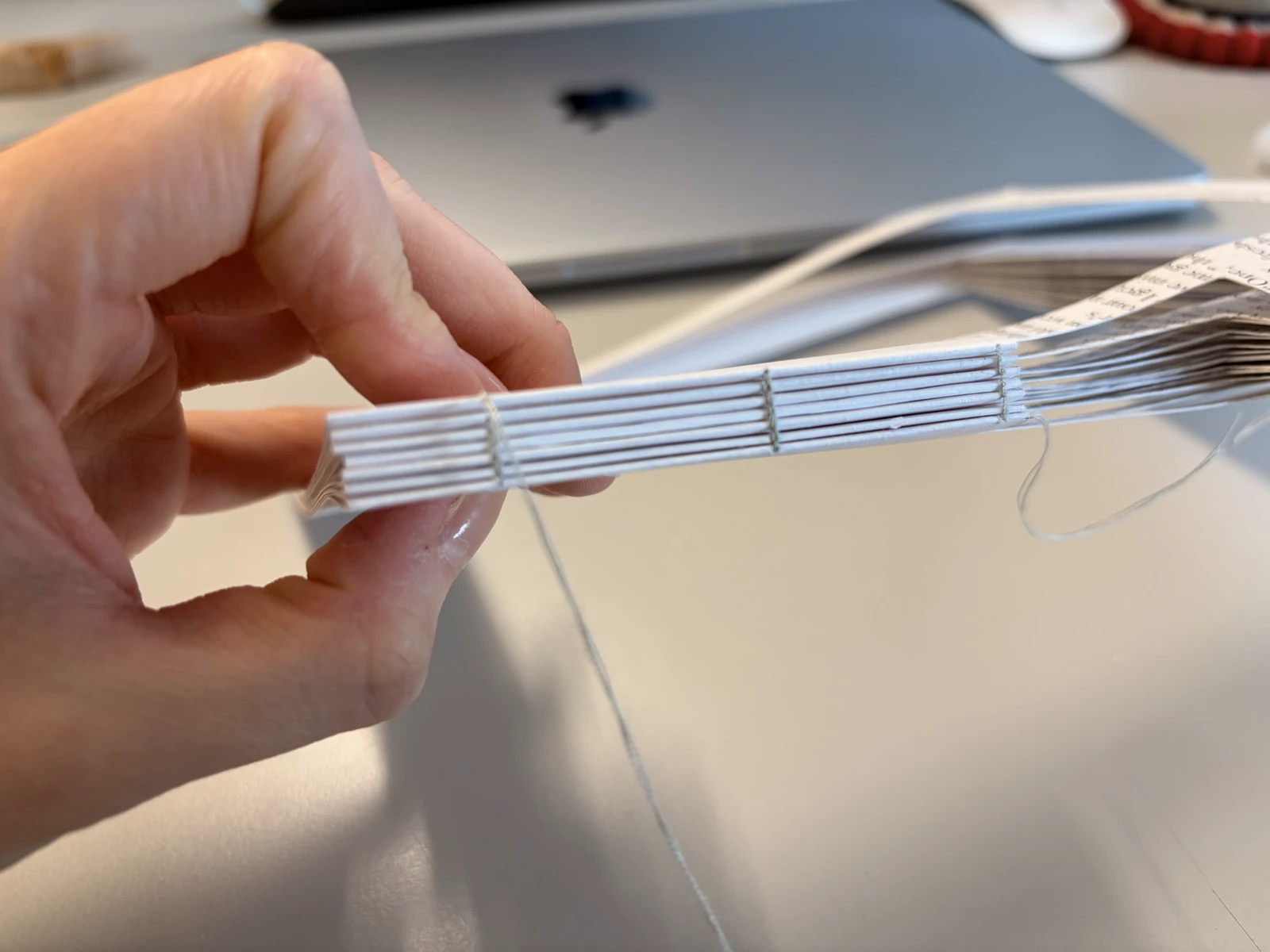 A hand holding the edge of the page block, its sewn signatures showing