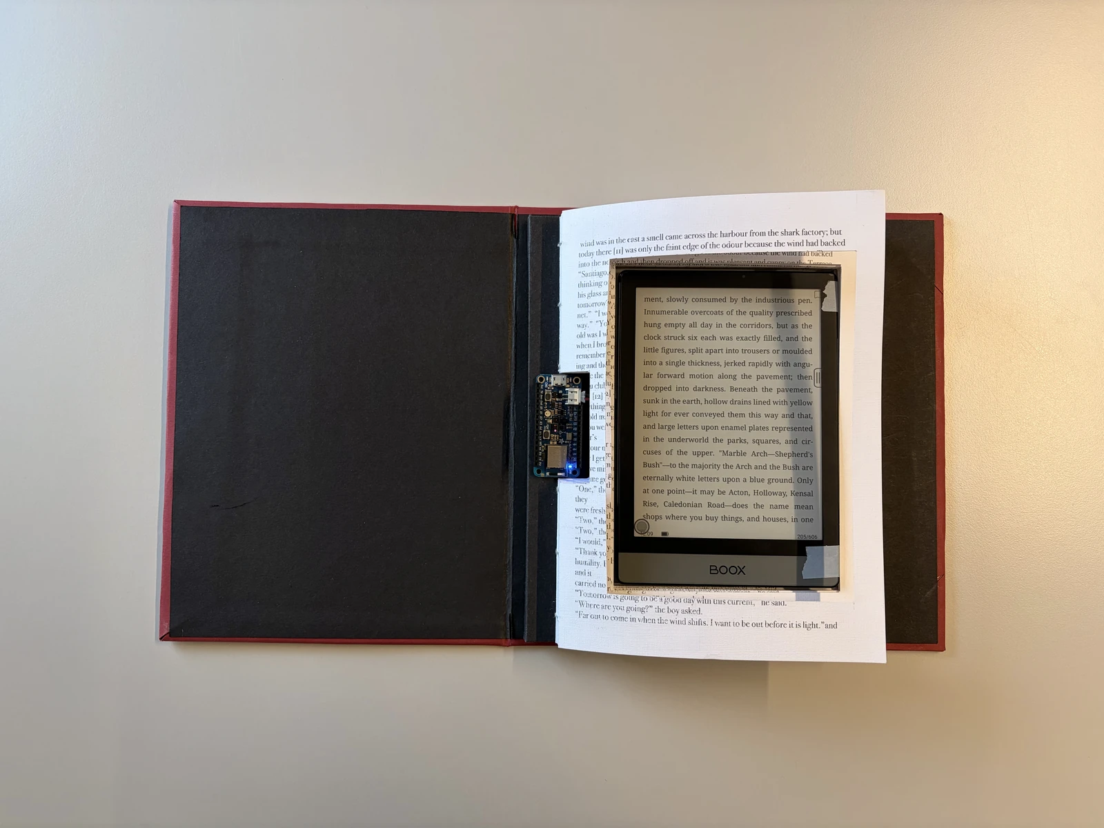 The finished book open on a table, an ebook reader inside the cut-out pages and the Arduino Feather at the spine