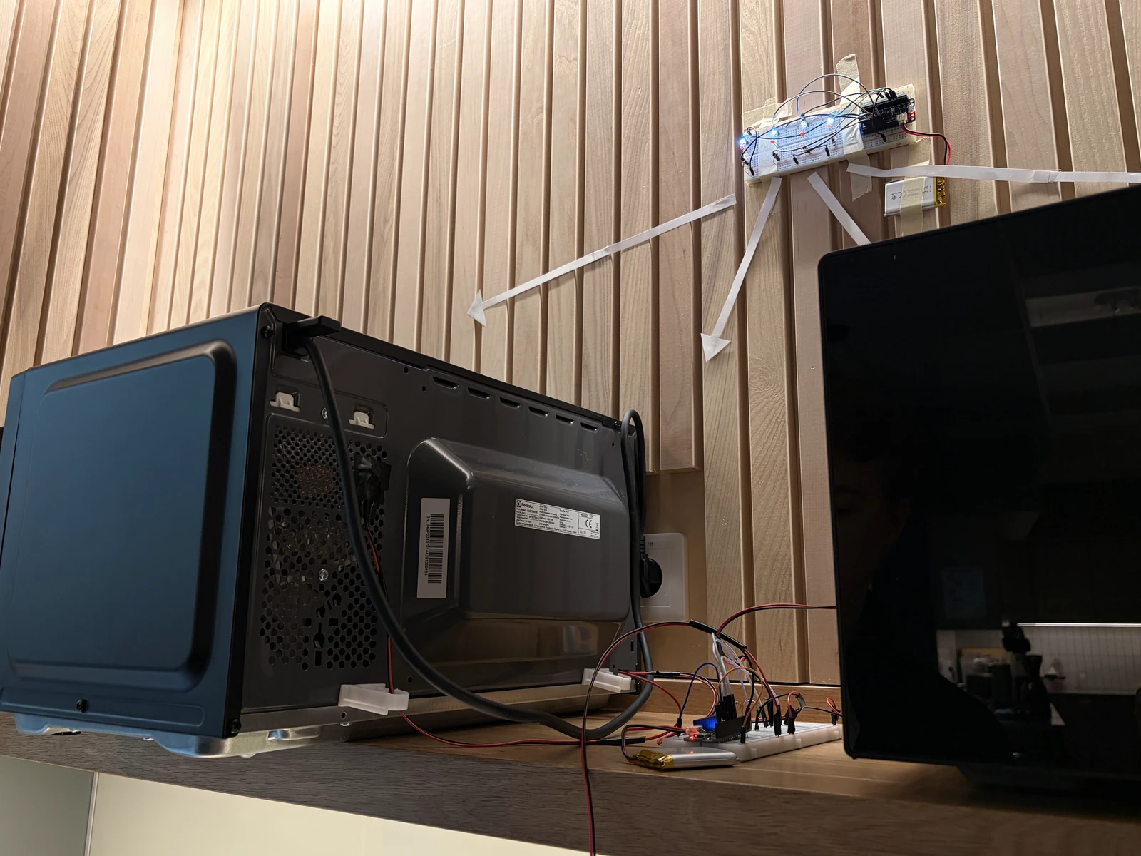 The whole setup: the panel on the wall above, the sensor breadboard on the counter beside the microwave